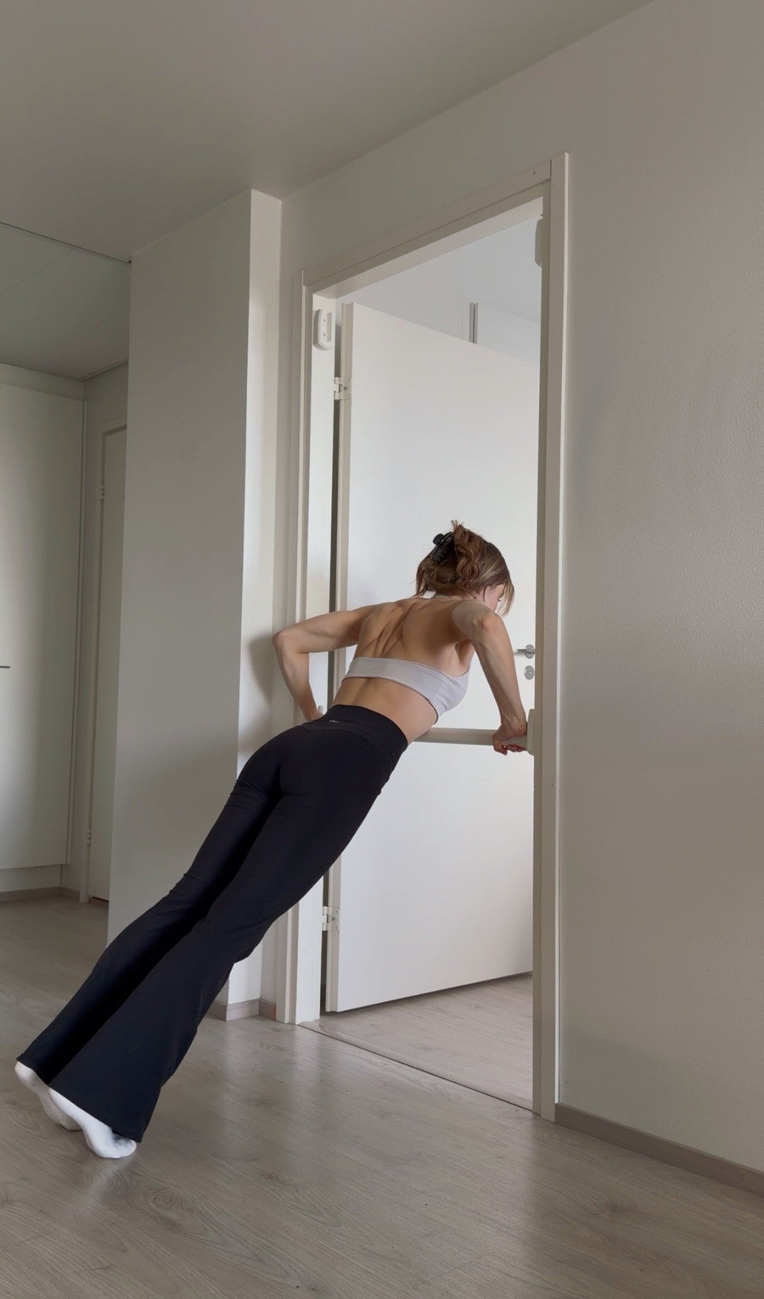 Person doing a push-up on a Pull-up Bar in a door frame in a minimalistic room.